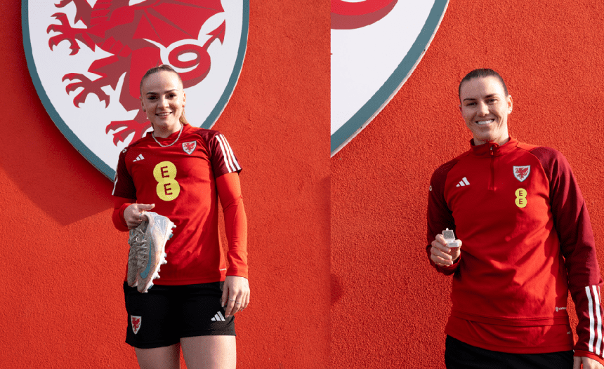 Wales Women players, Lily Woodham and Gemma Evans standing in front ofa red background withe FAW dragon logo on it, holidng the boots and the tooth they have donated to the museum.