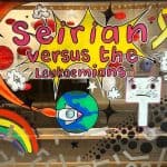 Celf ffenestr cartŵn llachar gan 'PaintedCreations by ME' (Michelle Edwards) ar gyfer arddangosfa 'Seirian versus the Leukamians' yn Nhŷ Pawb, Wrecsam