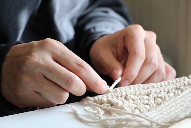 Dwylo oedolyn sy'n dysgu sut i wneud crefftau Macrame