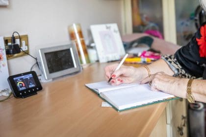 Older person leaning on a counter writing in a notebook, with a smart meter display on the left